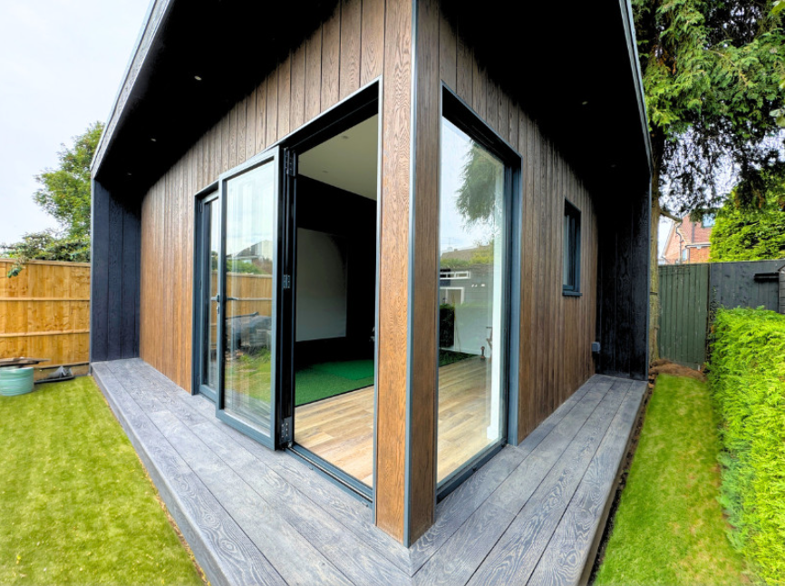 Modern house extension with large glass windows and wooden exterior on a sunny day.